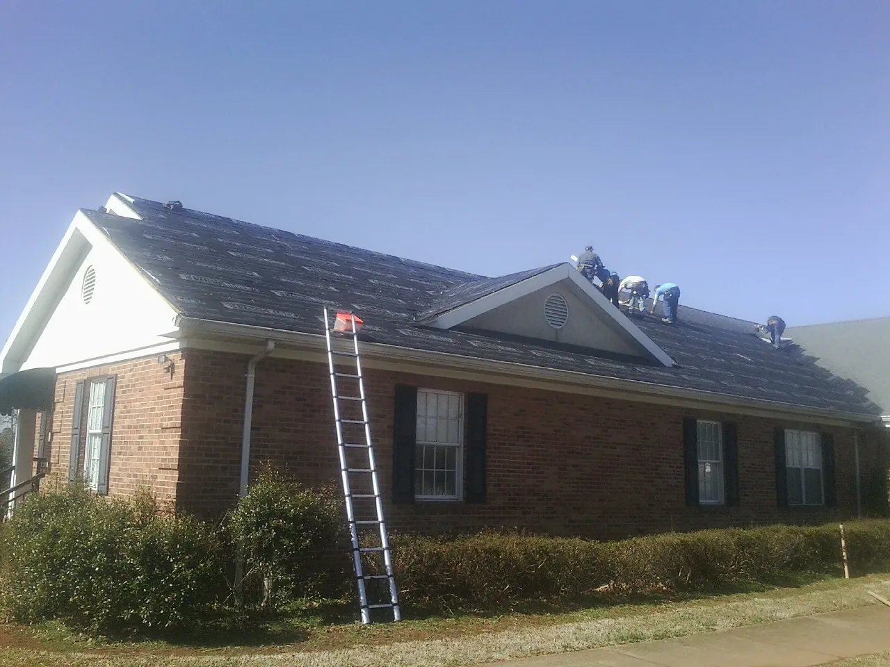 Crew tearing shingles off a brick ranch roof with a ladder set — Metal Roof Repair work by our crew in Oakley